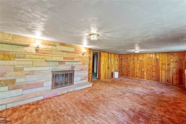 unfurnished living room featuring a stone fireplace, carpet flooring, a textured ceiling, and wooden walls