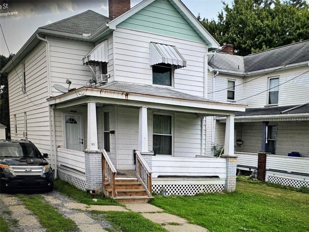 view of front facade with a front yard, driveway, roof with shingles, covered porch, and a chimney