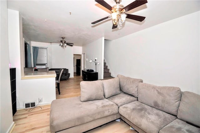 living area featuring visible vents, a ceiling fan, wood finished floors, and stairs