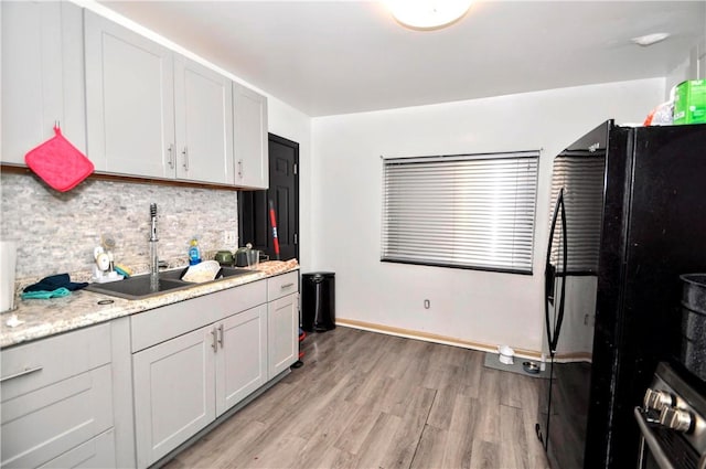 kitchen featuring wall oven, backsplash, light wood-type flooring, freestanding refrigerator, and a sink