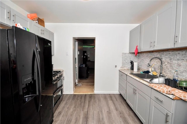 kitchen with light wood-style flooring, a sink, decorative backsplash, black appliances, and light countertops