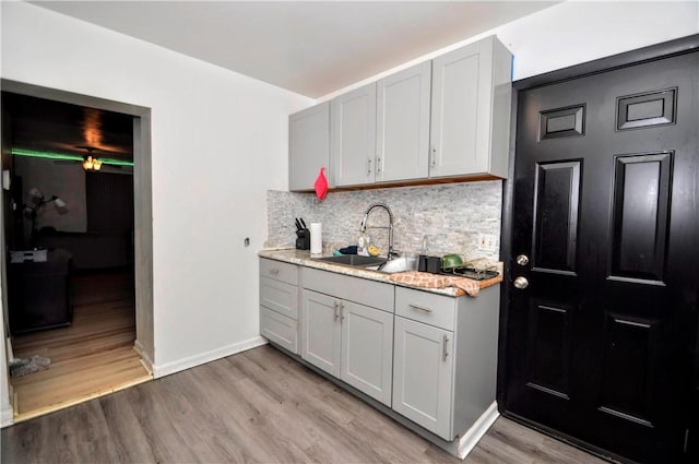 kitchen with baseboards, light wood finished floors, gray cabinets, a sink, and tasteful backsplash