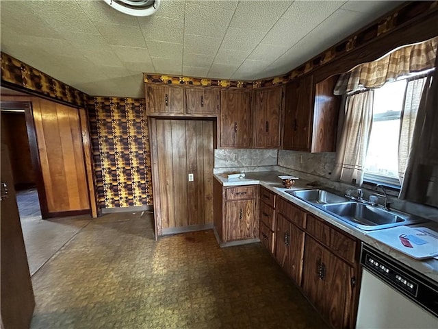 kitchen with wood walls, dishwasher, light countertops, decorative backsplash, and a sink