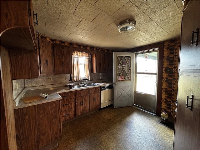 kitchen featuring dishwashing machine, dark floors, light countertops, and a sink