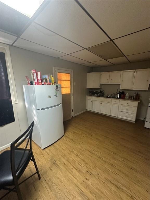 kitchen featuring baseboards, a drop ceiling, freestanding refrigerator, light wood-style floors, and white cabinetry