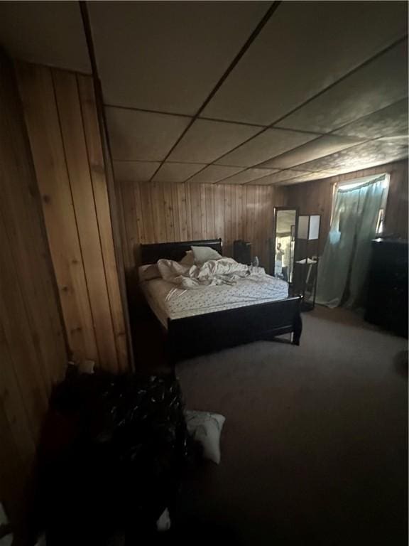 bedroom featuring carpet, a paneled ceiling, and wood walls