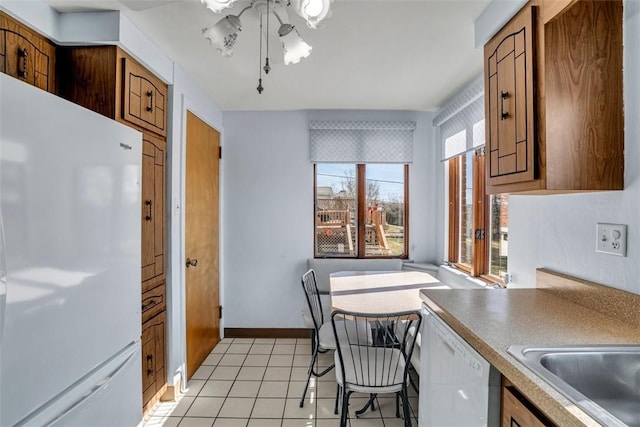 kitchen featuring white appliances, light tile patterned floors, brown cabinetry, and baseboards