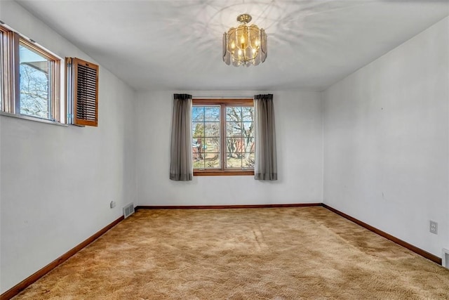 carpeted spare room with a wealth of natural light, visible vents, baseboards, and a chandelier