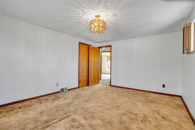 carpeted spare room with visible vents, baseboards, and a notable chandelier