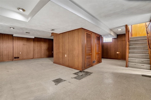 basement with stairs, wooden walls, visible vents, and carpet floors