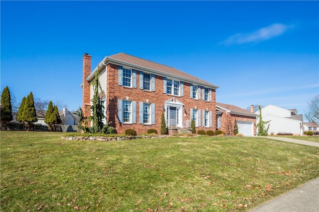 colonial-style house featuring driveway, a front yard, an attached garage, brick siding, and a chimney