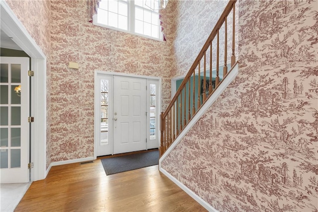 entrance foyer with wallpapered walls, a high ceiling, baseboards, and wood finished floors