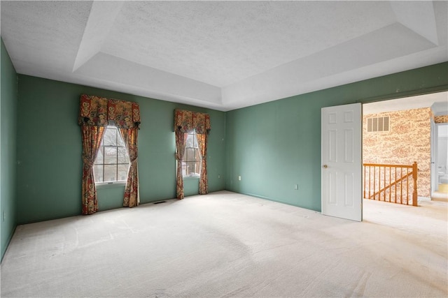 unfurnished room with a tray ceiling, carpet floors, a textured ceiling, and visible vents