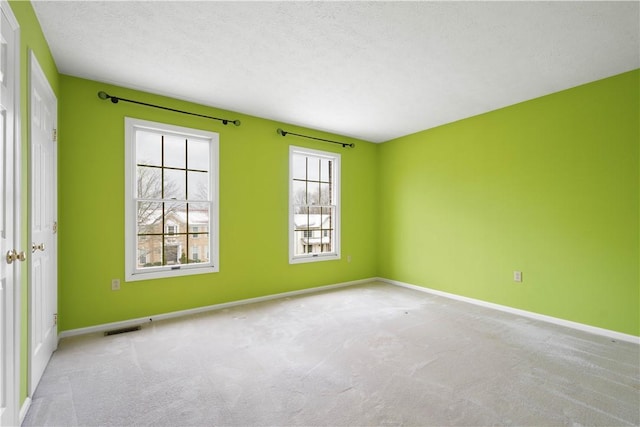 spare room featuring visible vents, a textured ceiling, baseboards, and carpet