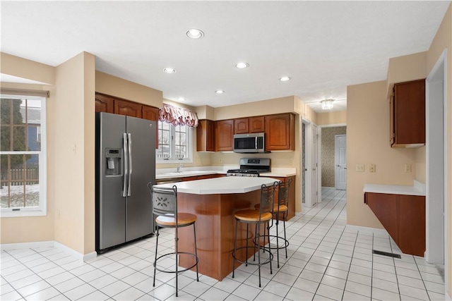 kitchen featuring a center island, a breakfast bar area, light countertops, light tile patterned floors, and appliances with stainless steel finishes