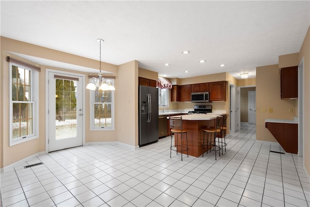 kitchen featuring a breakfast bar area, a kitchen island, light tile patterned flooring, light countertops, and appliances with stainless steel finishes