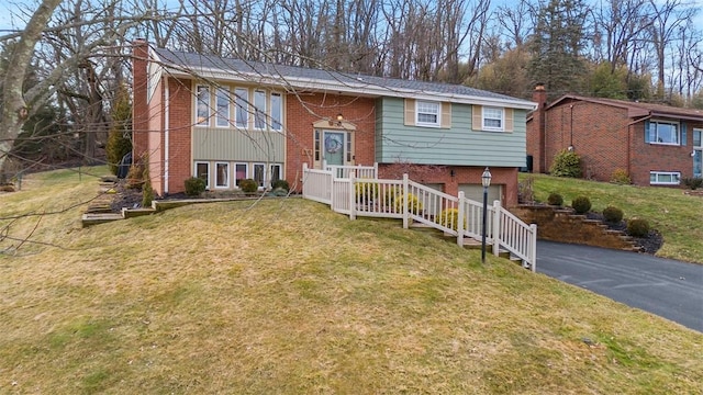 split foyer home featuring driveway, a front yard, a garage, brick siding, and a chimney