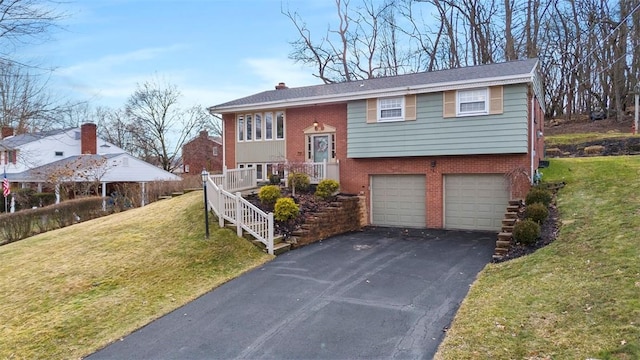 bi-level home with brick siding, a front lawn, a chimney, a garage, and driveway