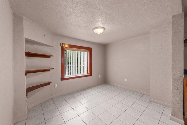 empty room with light tile patterned floors, a textured ceiling, baseboards, and a textured wall