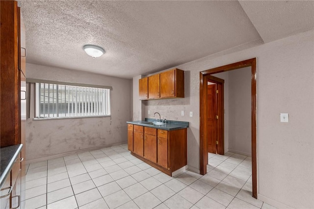 kitchen with light tile patterned floors, baseboards, a sink, dark countertops, and brown cabinets