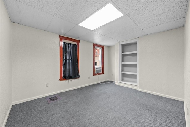 unfurnished room featuring visible vents, built in shelves, baseboards, dark carpet, and cooling unit