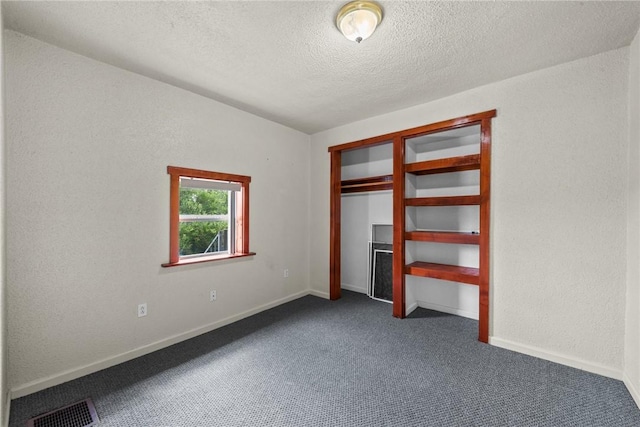 unfurnished bedroom with visible vents, a textured ceiling, dark colored carpet, baseboards, and a textured wall