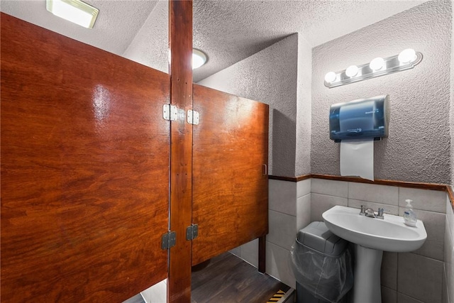 bathroom featuring a textured ceiling, tile walls, wood finished floors, and a textured wall