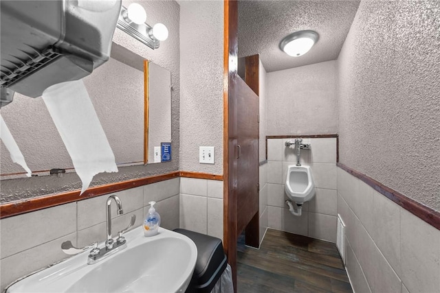 bathroom featuring wood finished floors, a textured ceiling, a textured wall, and a sink