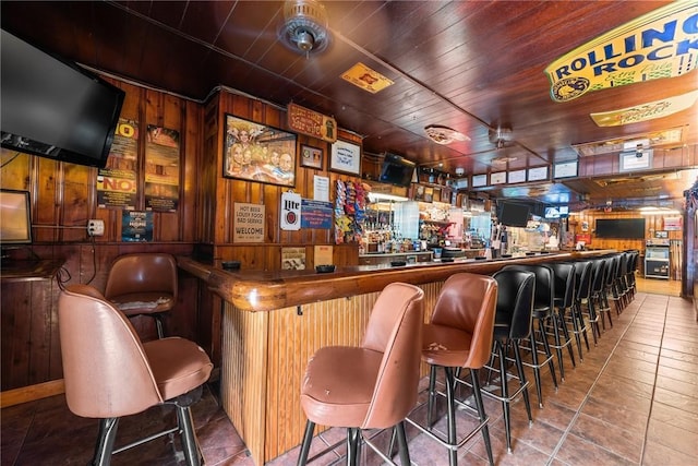 bar featuring tile patterned flooring, wooden walls, wooden ceiling, and a bar