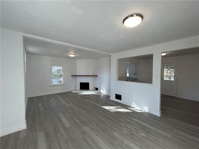 unfurnished living room featuring a healthy amount of sunlight, wood finished floors, baseboards, and a fireplace with raised hearth