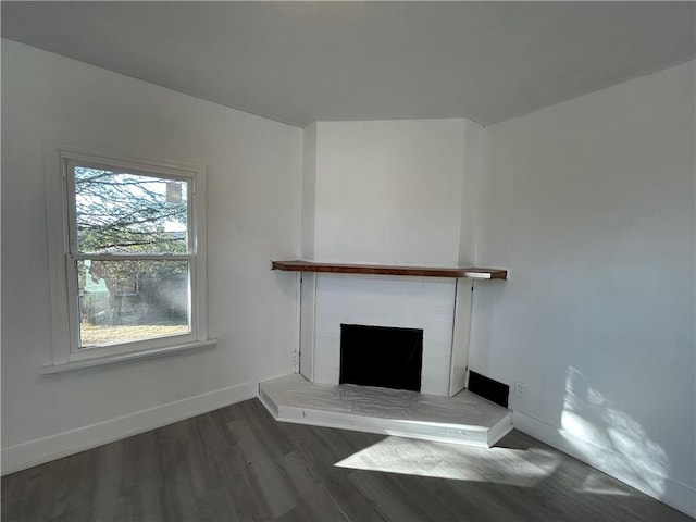 unfurnished living room featuring a brick fireplace, wood finished floors, and baseboards