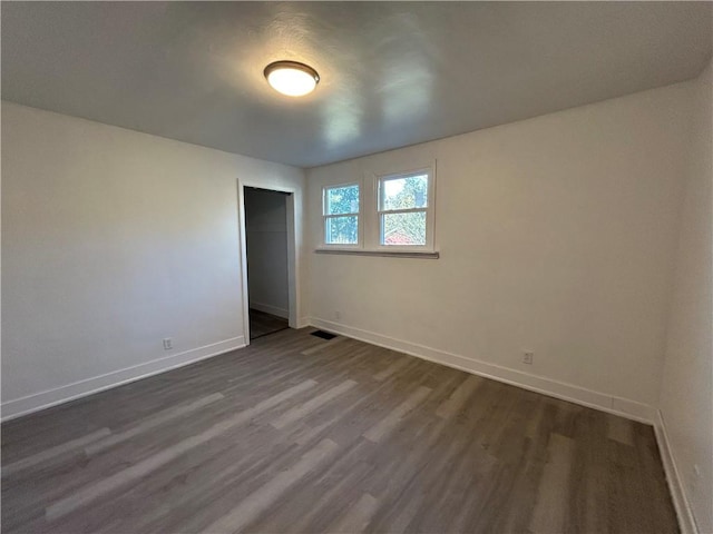 empty room with dark wood-style floors, visible vents, and baseboards