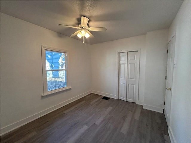 unfurnished bedroom with dark wood finished floors, baseboards, a closet, and ceiling fan