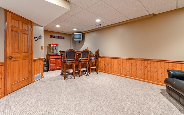 carpeted dining space with visible vents, wooden walls, a bar, and wainscoting