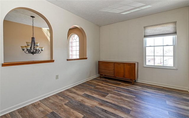 spare room with a notable chandelier, a textured ceiling, baseboards, and wood finished floors