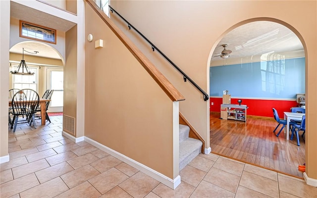 staircase featuring tile patterned flooring, arched walkways, baseboards, and ceiling fan