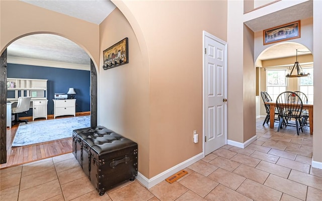 hallway featuring tile patterned floors, visible vents, baseboards, and arched walkways