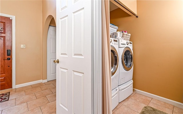 washroom with light tile patterned floors, baseboards, laundry area, arched walkways, and washer and clothes dryer