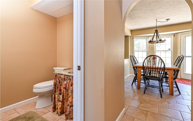 dining room with arched walkways, light tile patterned floors, a textured ceiling, and baseboards