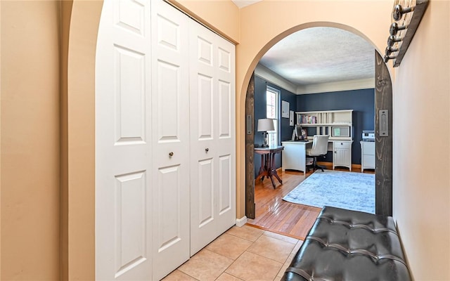 foyer entrance featuring arched walkways, ornamental molding, and light tile patterned flooring