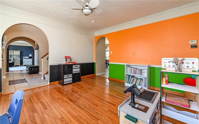 rec room featuring ornamental molding, a ceiling fan, a textured ceiling, wood finished floors, and arched walkways