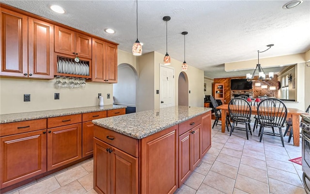 kitchen with light stone countertops, decorative light fixtures, brown cabinets, arched walkways, and a textured ceiling