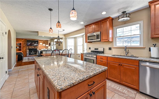 kitchen featuring a sink, a center island, a large fireplace, appliances with stainless steel finishes, and brown cabinetry