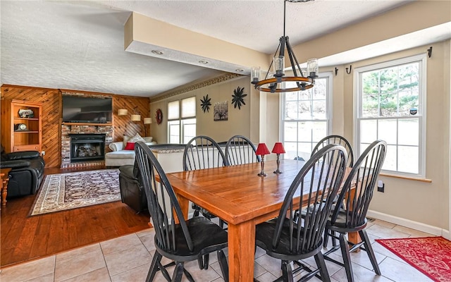 dining area featuring a textured ceiling, light tile patterned flooring, a fireplace, baseboards, and a chandelier