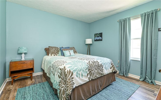 bedroom featuring baseboards, a textured ceiling, and wood finished floors