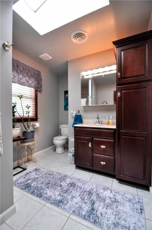 bathroom with toilet, a skylight, vanity, baseboards, and tile patterned flooring