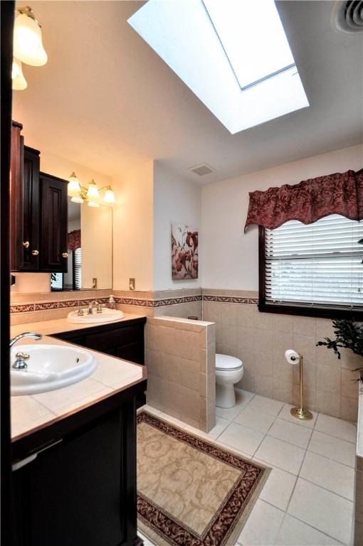 bathroom featuring tile patterned flooring, a wainscoted wall, toilet, vanity, and tile walls