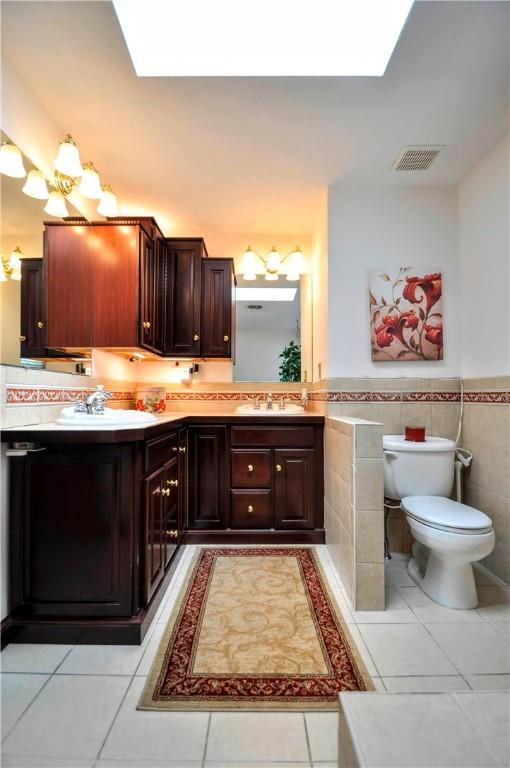 full bathroom with tile patterned flooring, tile walls, a skylight, and toilet