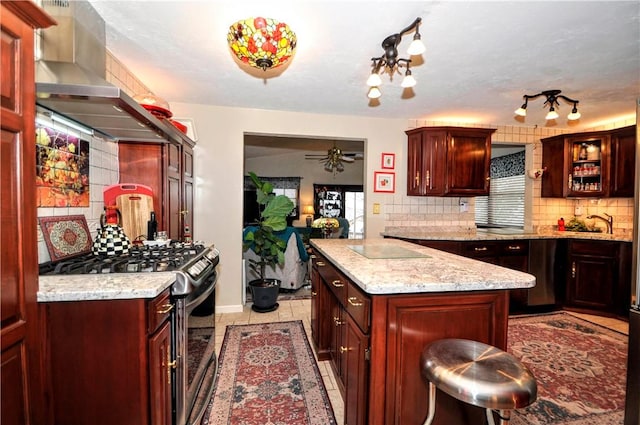 kitchen with reddish brown cabinets, stainless steel range with gas stovetop, and wall chimney range hood