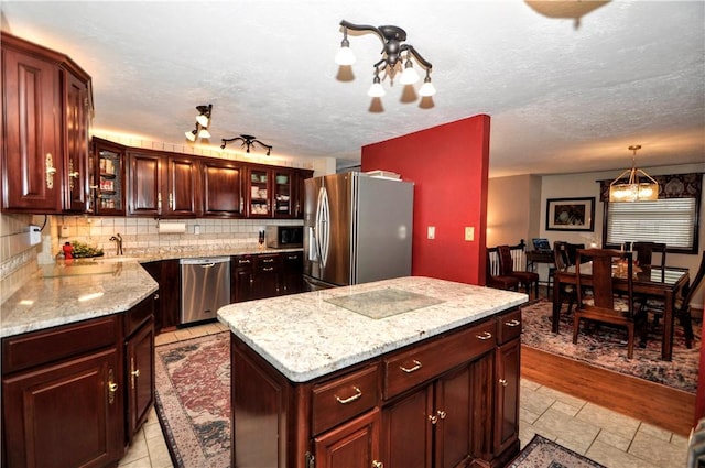 kitchen featuring decorative backsplash, glass insert cabinets, light stone countertops, a kitchen island, and appliances with stainless steel finishes
